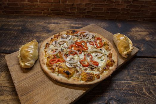 Traditional baked Argentine and Uruguay empanadas savoury pastries with meat beef stuffing against wooden background and pizza whit onion and red peppers.