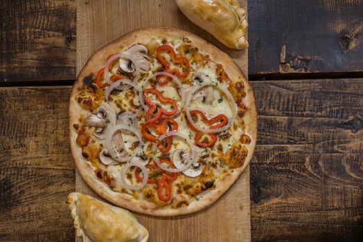 Traditional baked Argentine and Uruguay empanadas savoury pastries with meat beef stuffing against wooden background and pizza whit onion and red peppers.