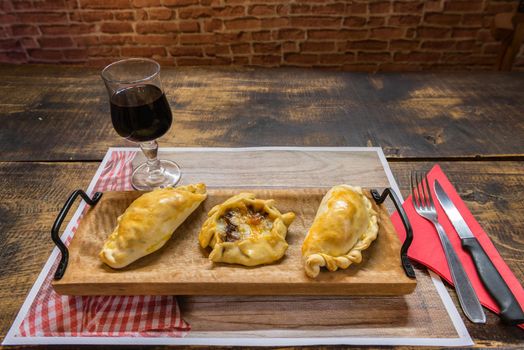 Traditional baked Argentine and Uruguay empanadas savoury pastries with meat beef stuffing against wooden background.