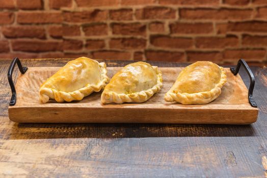Traditional baked Argentine and Uruguay empanadas savoury pastries with meat beef stuffing against wooden background.
