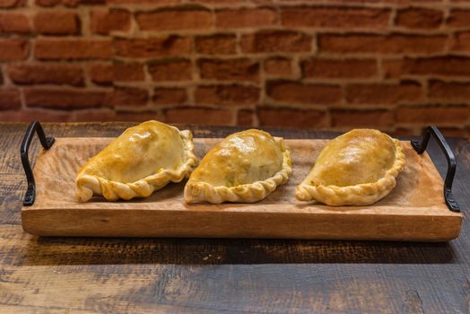 Traditional baked Argentine and Uruguay empanadas savoury pastries with meat beef stuffing against wooden background.
