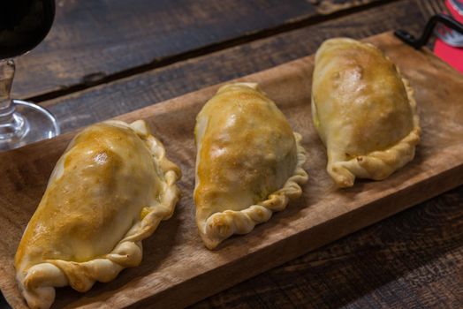 Traditional baked Argentine and Uruguay empanadas savoury pastries with meat beef stuffing against wooden background.