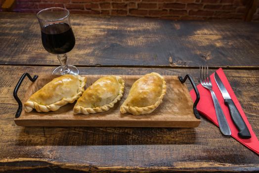 Traditional baked Argentine and Uruguay empanadas savoury pastries with meat beef stuffing against wooden background.