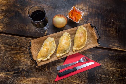 Traditional baked Argentine and Uruguay empanadas savoury pastries with meat beef stuffing against wooden background.