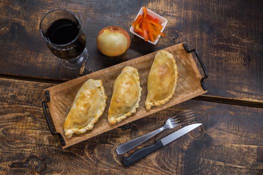 Traditional baked Argentine and Uruguay empanadas savoury pastries with meat beef stuffing against wooden background.