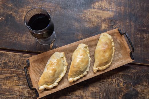 Traditional baked Argentine and Uruguay empanadas savoury pastries with meat beef stuffing against wooden background.