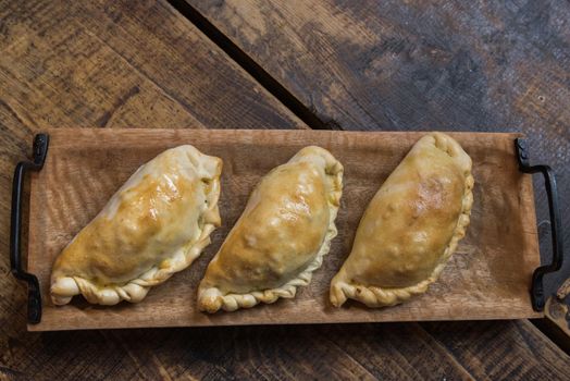 Traditional baked Argentine and Uruguay empanadas savoury pastries with meat beef stuffing against wooden background.