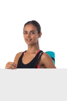Healthy hispanic fitness girl with rolled gymnastics yoga mat and blank banner isolated on white background