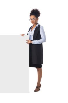 Friendly ethnic black business woman in formal wear in eyeglasses near blank banner isolated on white background, full length portrait