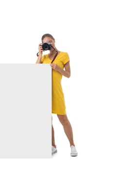 Full length portrait of young beautiful photographer girl with the camera and blank banner isolated on white background