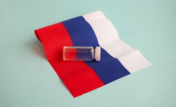 A bottle of the vaccine stands on a small flag of Russia. For the prevention, immunization and treatment of coronavirus infection. The concept of medicine and health care.