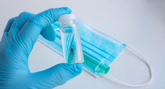 A blue-gloved hand holds a bottle of vaccine.The concept of coronavirus, medicine and medicines.