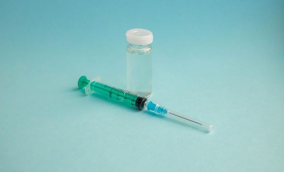 A syringe and a bottle of vaccine stand on a blue background. For the prevention, immunization and treatment of coronavirus infection. The concept of medicine and health care.