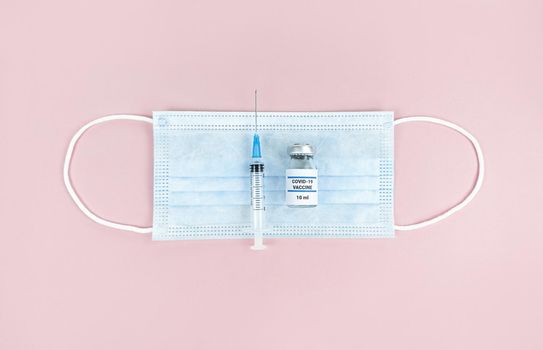 Syringe, medical bottle and face mask on a pink background.