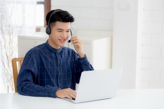 Young asian businessman working on laptop computer wearing headphone at home, business man wearing headset for video conference, communication and education, male study and learning for e-learning.