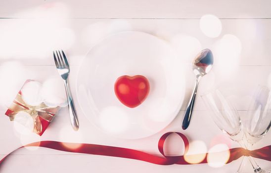 Valentine day concept, wineglass and red ribbon and utensil put in heart on white wooden table background with bokeh, champaign glass on wood desk, couples wine glass together, holiday concept.