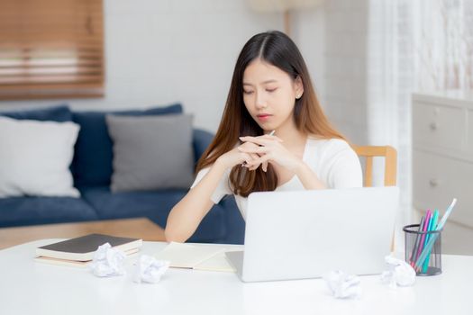 Young asian woman working with laptop computer think idea project and paper crumpled having problem on table at home, girl using notebook with frustrated and trouble, business and freelance concept.