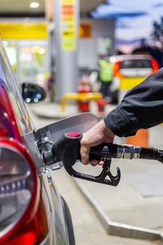 granddad's hand in black jacket refueling gray metallic car on gas station at night - close-up with selective focus and background blur