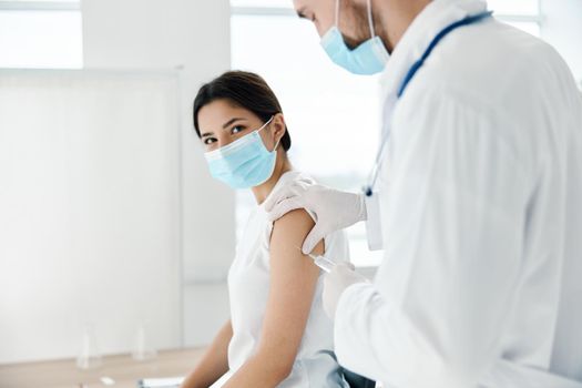 woman in hospital in medical mask and doctor with syringe vaccination epidemic infection. High quality photo