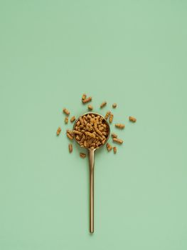 Buckwheat tea in spoon on light green background. Top view of healthy ku qiao or soba tea groats over green paper background. Minimal flat lay tartary buckwheat seeds. Copy space. Vertical