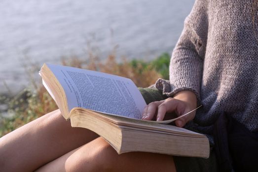 Young Woman Reading Book While Sitting Outdoors, close-up view