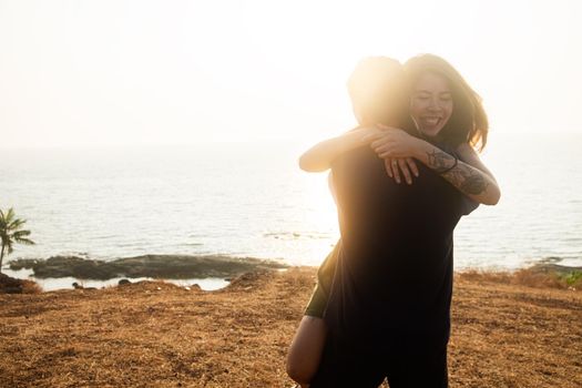 Backlit Portrait of a young romantic couple swirls in a hug against the backdrop of the sea. Anjuna Hills, Goa, India