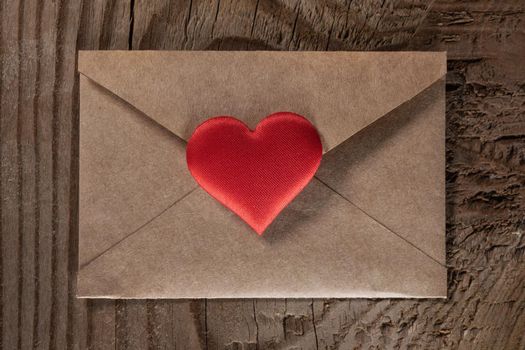 Valentine day love letter, envelope of craft paper with red heart on wooden background