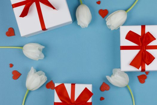 White tulip flowers red hearts and gifts composition on blue background top view with copy space. Valentine's day, birthday, wedding, Mother's day concept. Copy space