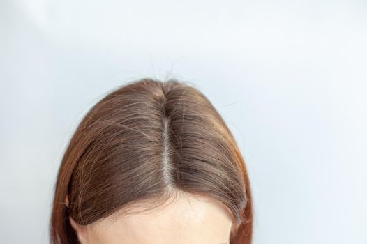 A woman's head with a parting of gray hair that has grown roots due to quarantine. Brown hair on a woman's head close-up.