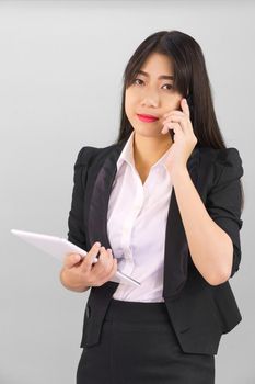 Young Asian women in suit standing using her digital tablet and phone against gray background