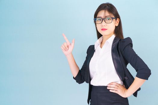 Asian business woman in suit with finger pointing up on blue background