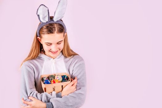 Girl in rabbit bunny ears on head with basket full colored eggs on pink background. Cheerful smiling happy child. Easter holiday banner