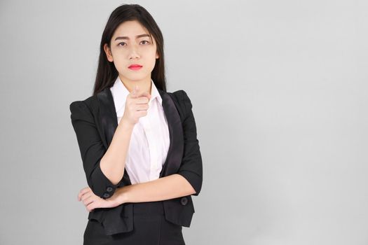 Asian woman in suit looking at camera and pointing finger on gray background