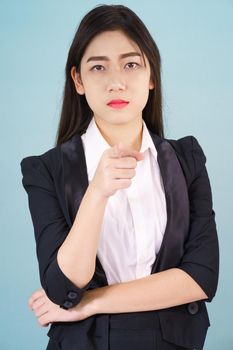 Asian woman looking at camera and pointing finger on blue background