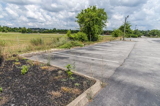 Horizontal shot of the empty overgrown parking lot of a bankrupt retail business after the Pandemic.
