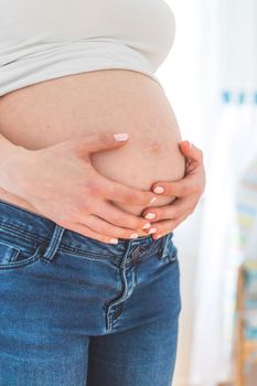 Caucasian pregnant mother touching her naked tummy, blue jeans, close up