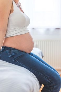 Caucasian pregnant mother touching her naked tummy, blue jeans, close up