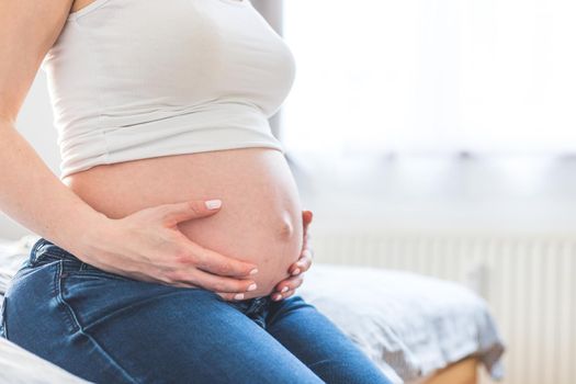 Caucasian pregnant mother touching her naked tummy, blue jeans, close up