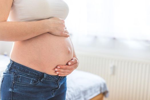 Caucasian pregnant mother touching her naked tummy, blue jeans, close up