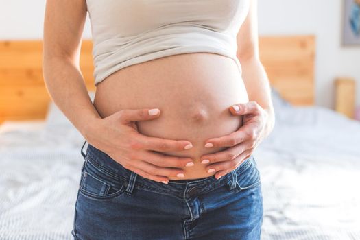 Caucasian pregnant mother touching her naked tummy, blue jeans, close up