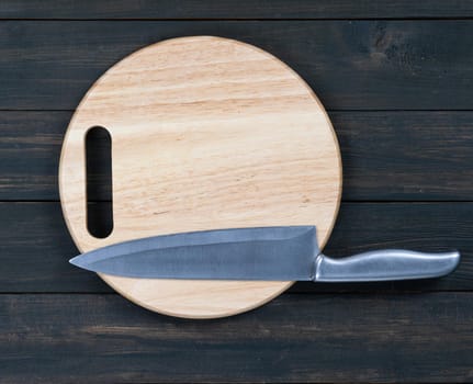 Close up kitchen knife and wooden round empty cutting board on a wooden table