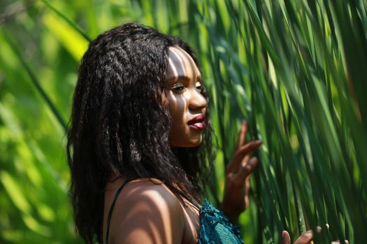 Cheerful young woman standing among tropical leaf.