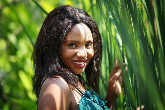 Cheerful young woman standing among tropical leaf.