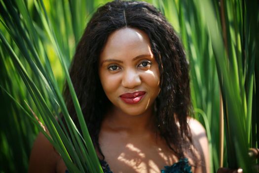 Cheerful young woman standing among tropical leaf.