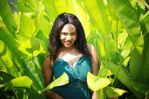 Cheerful young woman standing among tropical leaf.