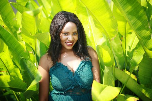 Cheerful young woman standing among tropical leaf.