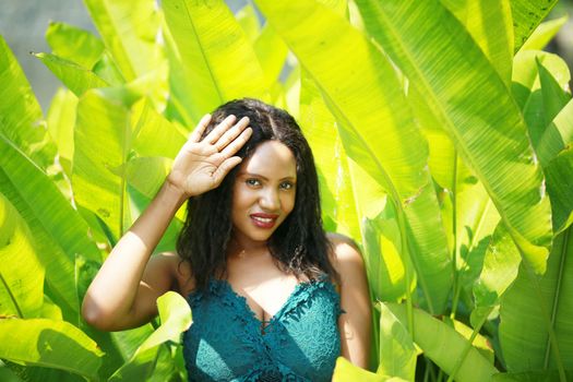 Cheerful young woman standing among tropical leaf.