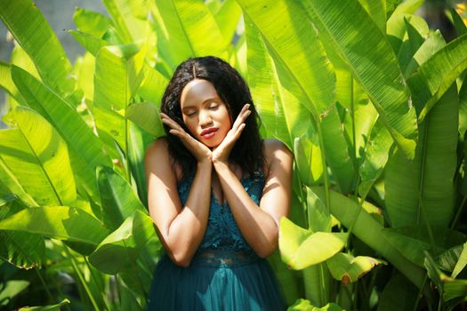 Cheerful young woman standing among tropical leaf.