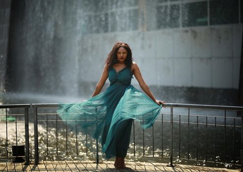 Cheerful young woman standing outdoor against water park in the garden.