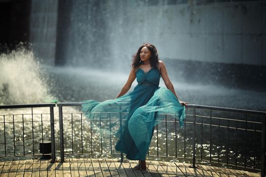 Cheerful young woman standing outdoor against water park in the garden.